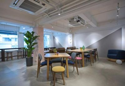 Spacious open-plan lounge with assorted wooden tables, colorful chairs, and indoor plants.