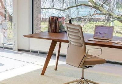 Bright private workspace with a wooden desk, ergonomic chair, and large windows overlooking trees.