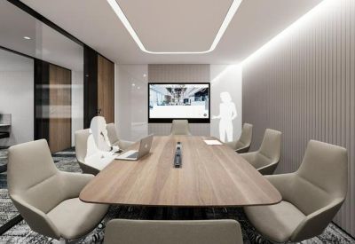 Bright meeting room with a large wooden table, comfortable grey chairs, and integrated video conferencing.
