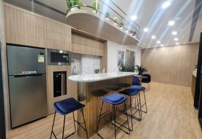 Communal kitchen and breakout area with a marble island, blue velvet stools, and wooden cabinetry.