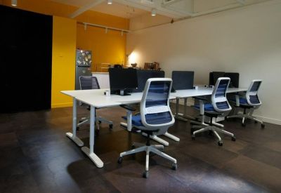 Open-plan office with white desks, ergonomic chairs, and a yellow feature wall.