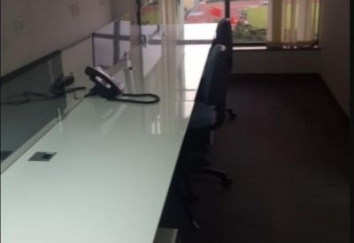 Long white communal workstation desk in a bright room with a view of the city skyline.