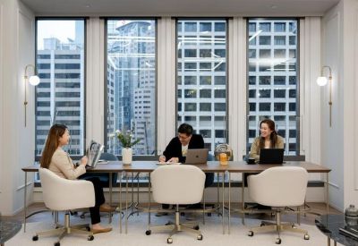 Professionals working at a long wooden communal table in front of city-view windows.