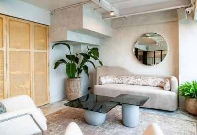 Bright breakout lounge with a curved sofa, round mirror, and large potted plants.