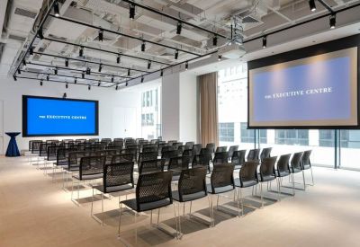 Large conference hall with rows of black chairs and two large projection screens.