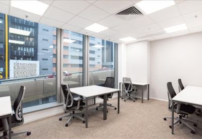 Bright corner office with multiple desks, ergonomic chairs, and large windows.