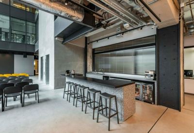 Sleek communal break area with a long marble-topped bar, black stools, and exposed ceiling pipes.