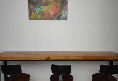 Wooden breakfast bar with three stools and a small abstract artwork on a white wall.