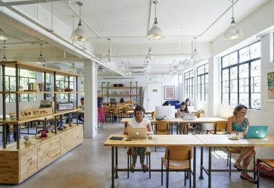 Bright, open-plan coworking space with long wooden desks and large windows.