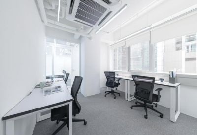 Bright shared office space with long white desks and ergonomic black chairs.