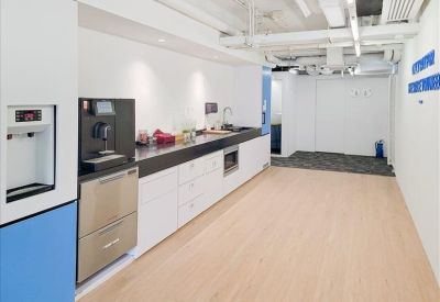 Modern office pantry and refreshment area with white cabinetry and wood flooring.
