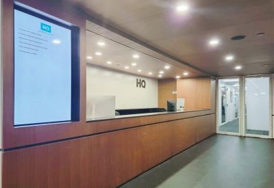 Professional reception area with a long wood-fronted desk and a digital information screen.