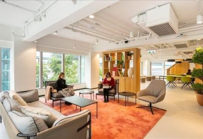 Spacious communal lounge featuring an orange rug, grey seating, and large windows with greenery.