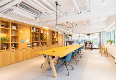 Open-plan coworking area with a long wooden table, blue chairs, and a floor-to-ceiling bookshelf.