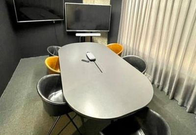 Small meeting room featuring an oval table, two wall-mounted screens, and dark acoustic walls.