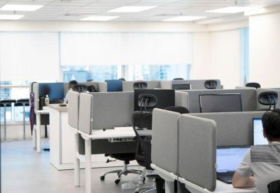 Modern open-plan office with multiple workstations, grey partitions, and ergonomic chairs.