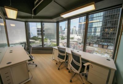 Bright corner office with multiple desks and panoramic floor-to-ceiling city views.