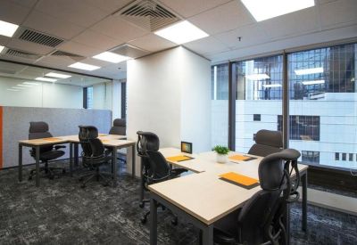 Bright corner office with multiple L-shaped desks and city window views.