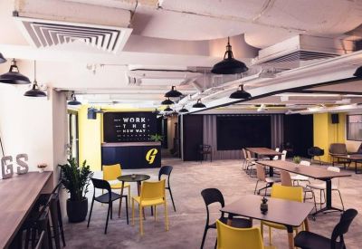 Vibrant communal coworking space with yellow and black chairs, indoor plants, and a reception desk.