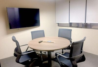 Small meeting room featuring a round wooden table, four black mesh chairs, and a wall-mounted TV.