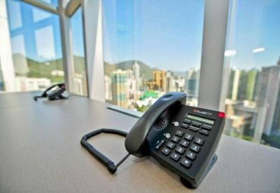 Close-up of a black office telephone on a desk overlooking a sunny city skyline.