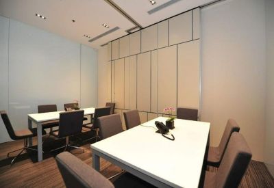 Bright conference room with two large white tables and grey cushioned chairs.