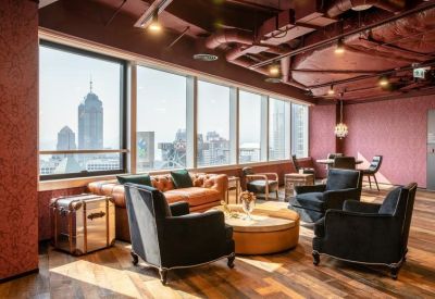 Bright communal lounge with pink patterned walls, plush armchairs, and floor-to-ceiling city views.