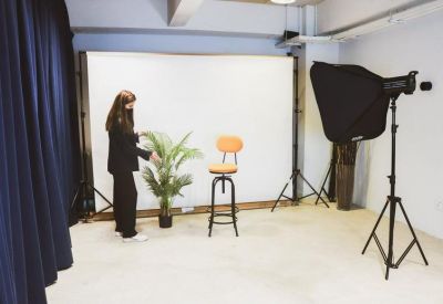 Photography studio setup with a white backdrop, lighting equipment, and an orange stool.