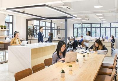 Spacious open-plan coworking area with long wooden tables and ample natural light.