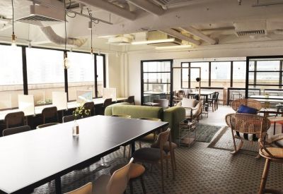 Open-plan coworking space with long black tables, windows, and a green sofa divider.