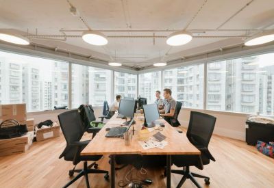 Open-plan office space with wooden desks and black ergonomic chairs overlooking the city.