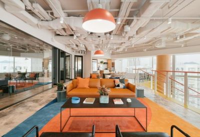 Modern breakout area with a brown leather sofa, orange carpet, and exposed ceiling pipes.