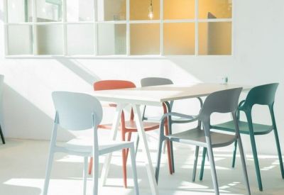 Minimalist meeting table with colorful chairs set against a bright window and white grid partition.