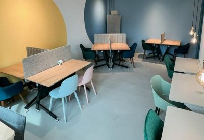 Spacious breakout area with light wood tables, colorful seating, and a large yellow wall graphic.