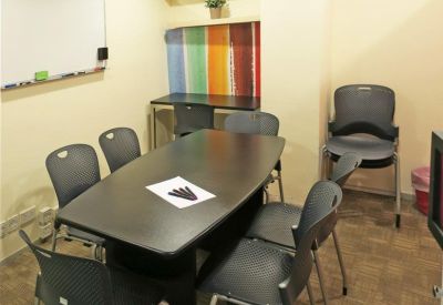 Meeting room featuring a dark oval table, grey chairs, and a colourful striped feature wall.