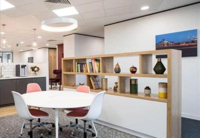 Modern breakout space with a round white table, pink chairs, and a light wood shelving unit.