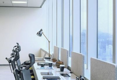 Row of modern office desks with ergonomic chairs alongside floor-to-ceiling windows.
