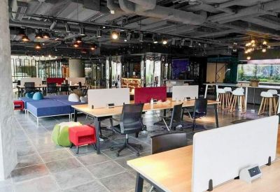 Open-plan office space featuring industrial ceilings, wooden desks, and colorful beanbags.