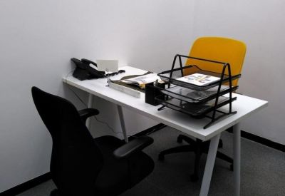 Compact private office featuring a white desk, ergonomic black chair, and a bright yellow visitor chair.