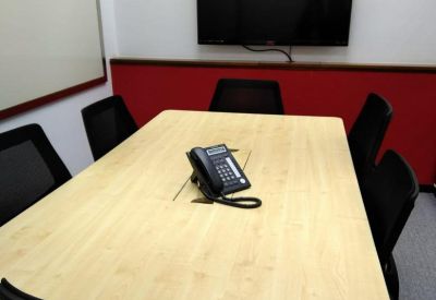 Private meeting room with a light wood table, black chairs, and a large wall-mounted screen.