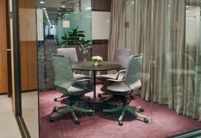Small meeting room with grey chairs and a round table behind a glass partition.
