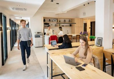 Bright coworking area with wooden desks, a printer station, and people working.