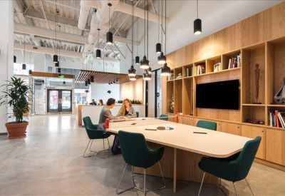 Conference room featuring a large light-colored table, teal chairs, and wood shelving.
