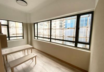 Spacious office area with a long wooden table, bench, and large windows providing natural light.