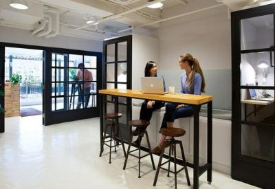 Bright coworking area with a high-top wooden table, stools, and private phone booths.