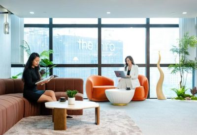 Sunlit lounge area with orange armchairs and a brown sectional sofa.