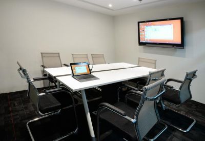 Professional meeting room featuring a white conference table, mesh chairs, and a wall-mounted monitor.