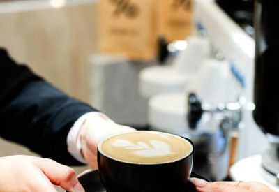 Close-up of a barista serving a latte with coffee beans in the background.