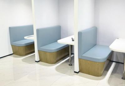 Modern breakout area featuring semi-private blue booths and white tables.