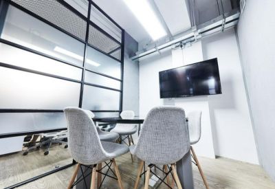 Modern meeting room with a glass partition, large TV screen, and grey bucket chairs.